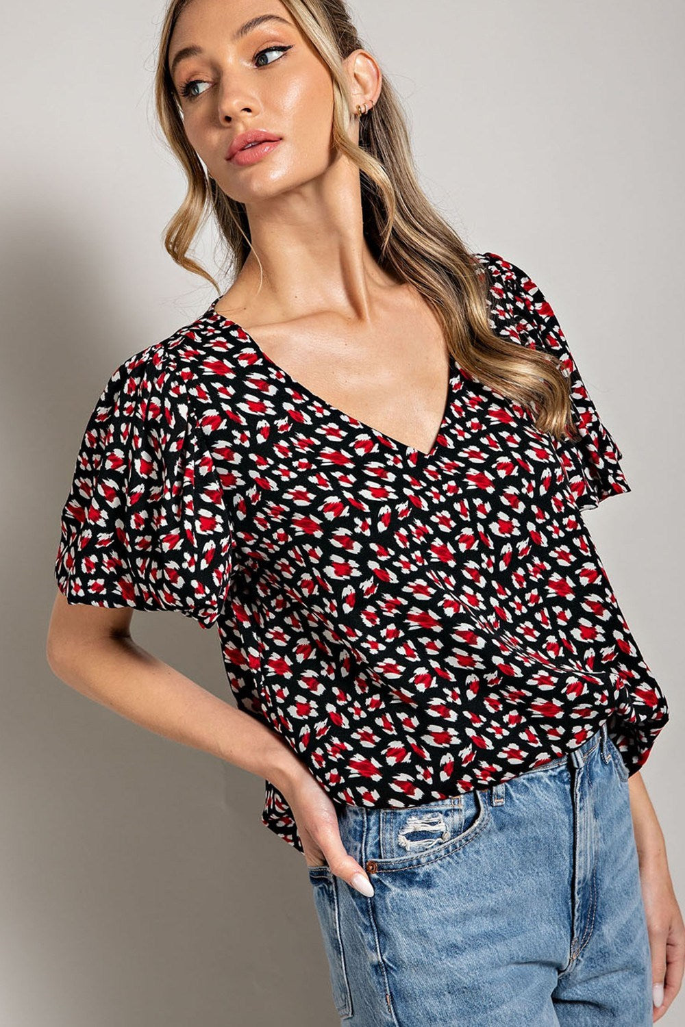 Woman wearing a patterned top and jeans against a neutral background