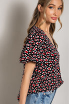 Woman wearing a black patterned blouse with blue jeans against a neutral background