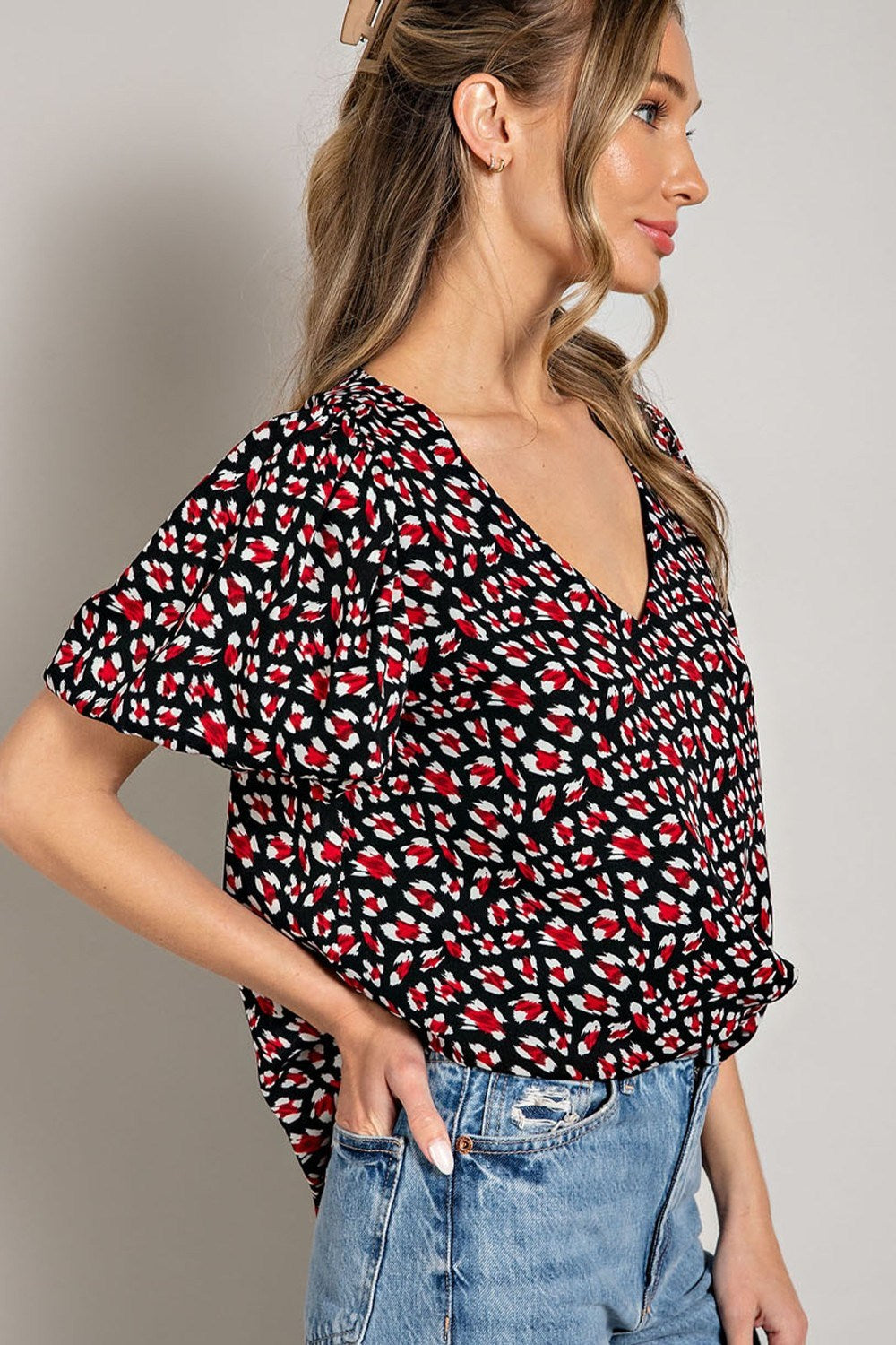 Woman wearing a black floral patterned top with blue jeans on a plain background