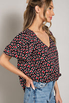 Woman wearing a black floral patterned top with blue jeans on a plain background