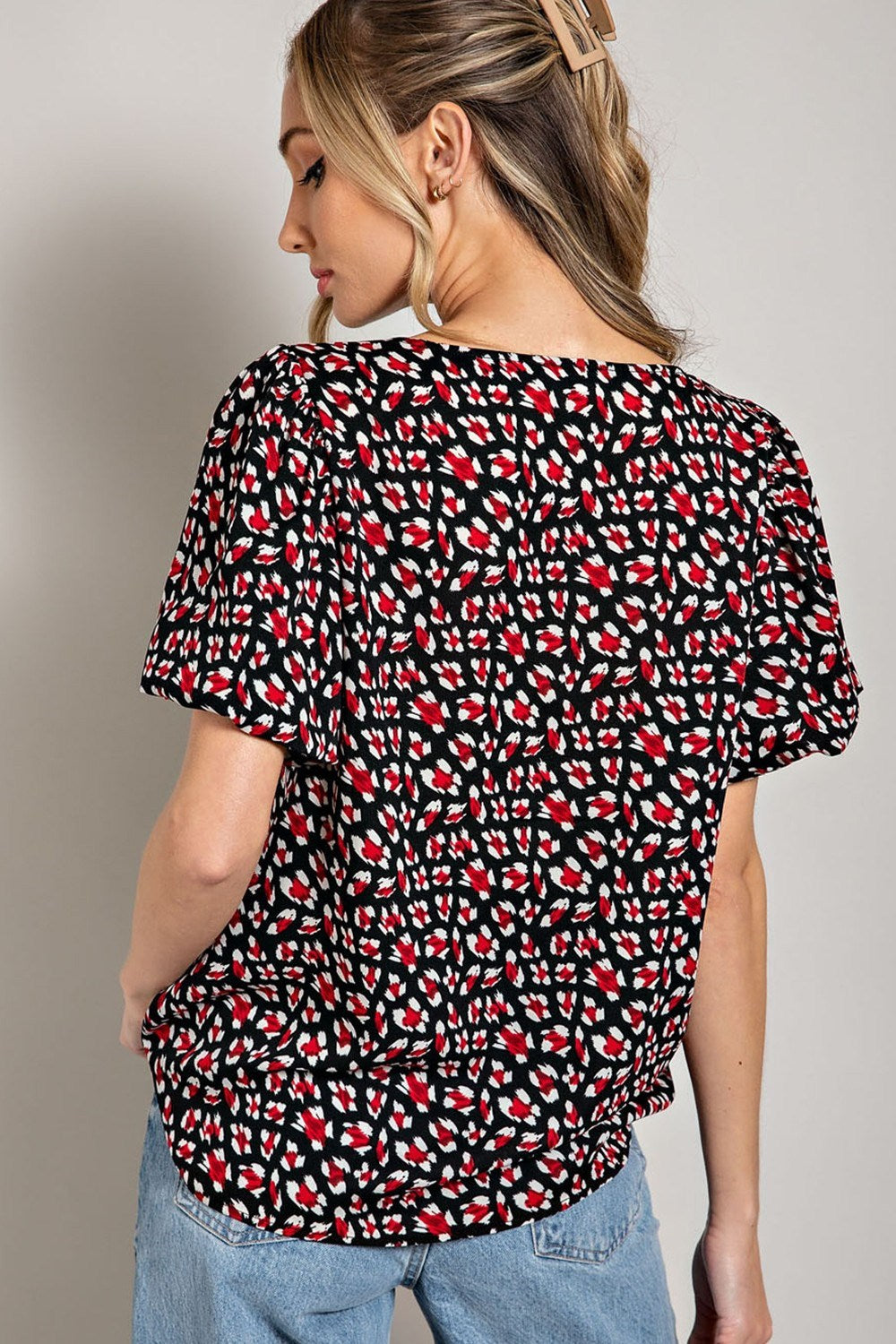 Woman wearing a black blouse with red and white abstract pattern on a plain background
