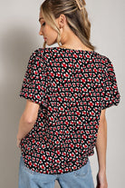 Woman wearing a black blouse with red and white abstract pattern on a plain background