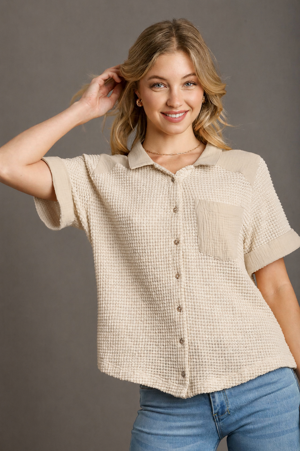 Woman wearing a beige checkered shirt and blue jeans against a gray background