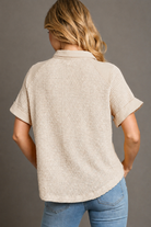 Woman wearing a beige textured shirt and blue jeans against a gray background