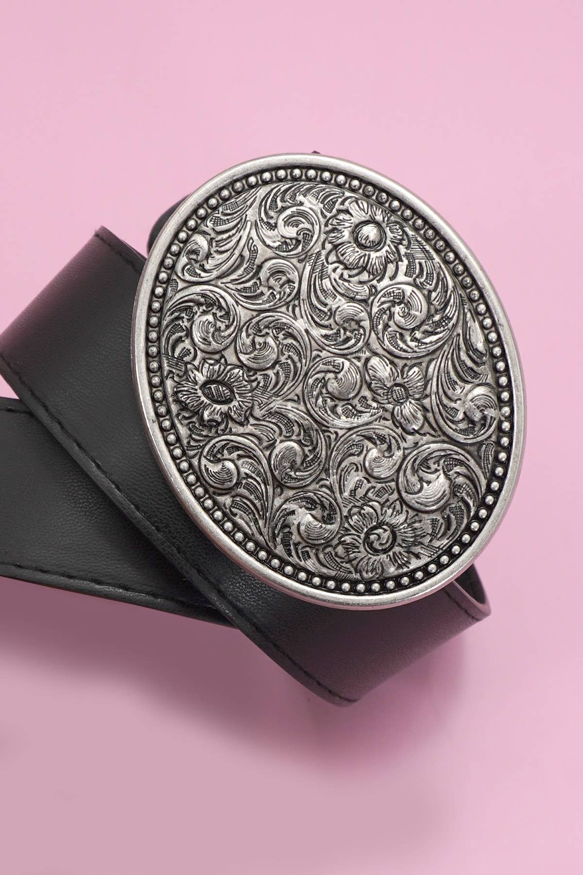 Decorative silver belt buckle on a black belt against a pink background