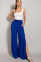 Woman wearing a white top and blue wide-leg pants on a plain background