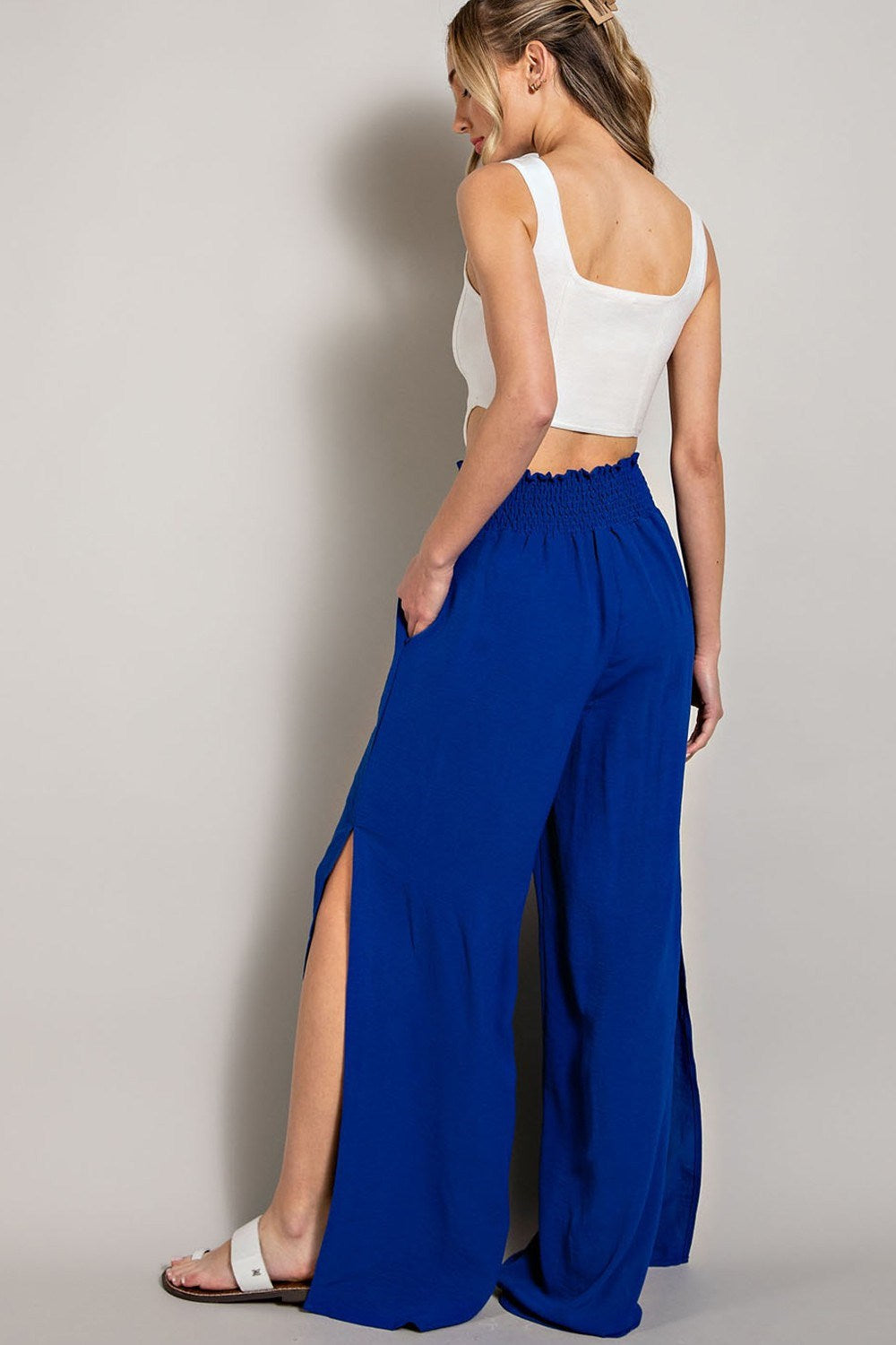 Woman wearing a white top and blue high-waisted pants against a plain background