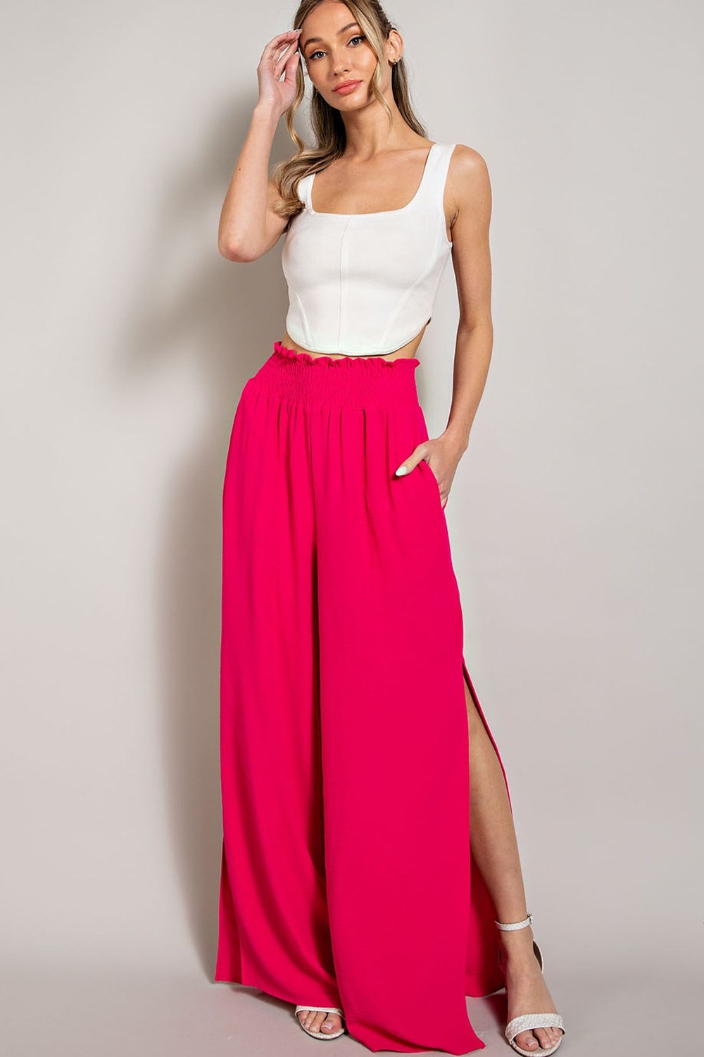 Woman wearing a white top and bright pink wide-leg pants on a plain background