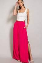 Woman wearing a white top and bright pink wide-leg pants on a plain background