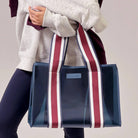 Person holding a blue tote bag with red and white stripes on a plain background