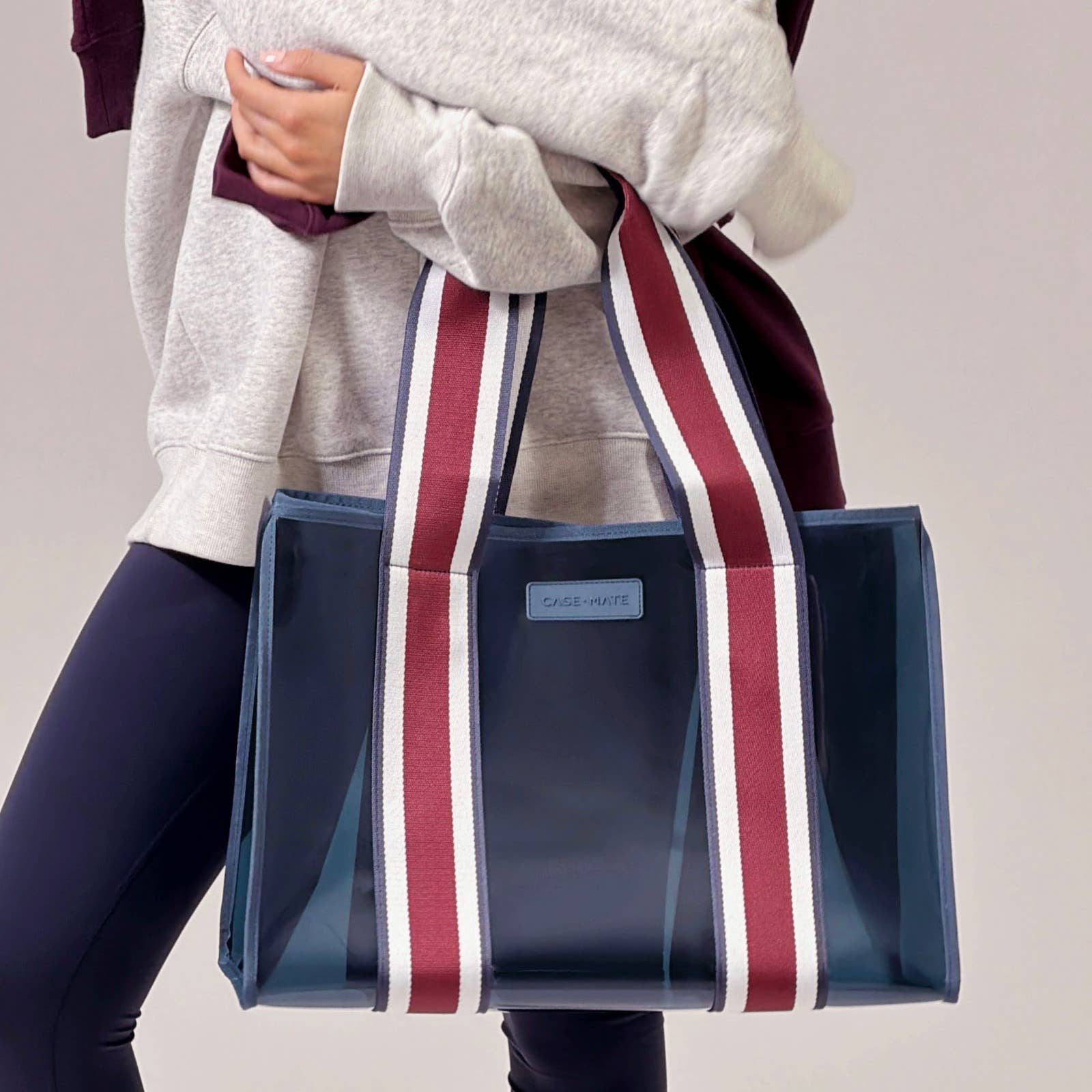 Person holding a blue tote bag with red and white stripes on a plain background