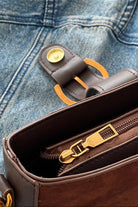 Brown leather wallet with gold zipper pull on a blue denim background