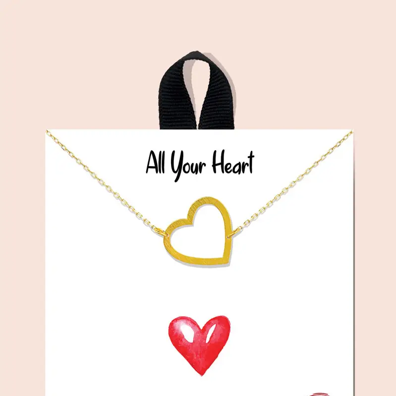 A gold open-heart necklace displayed on a white jewelry card with the text 'All Your Heart' and a red heart illustration, set against a pale pink background with a black ribbon loop at the top.