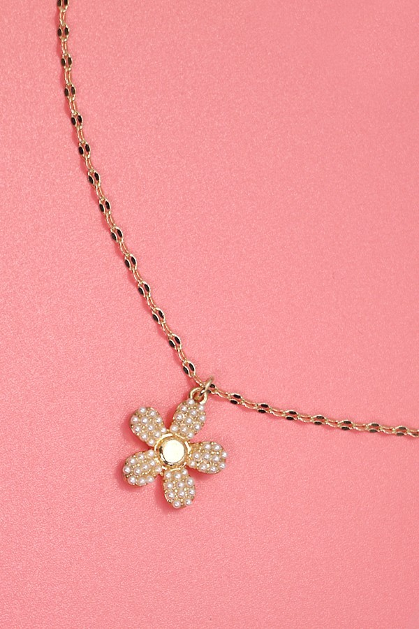 Gold flower-shaped pendant necklace on a pink background