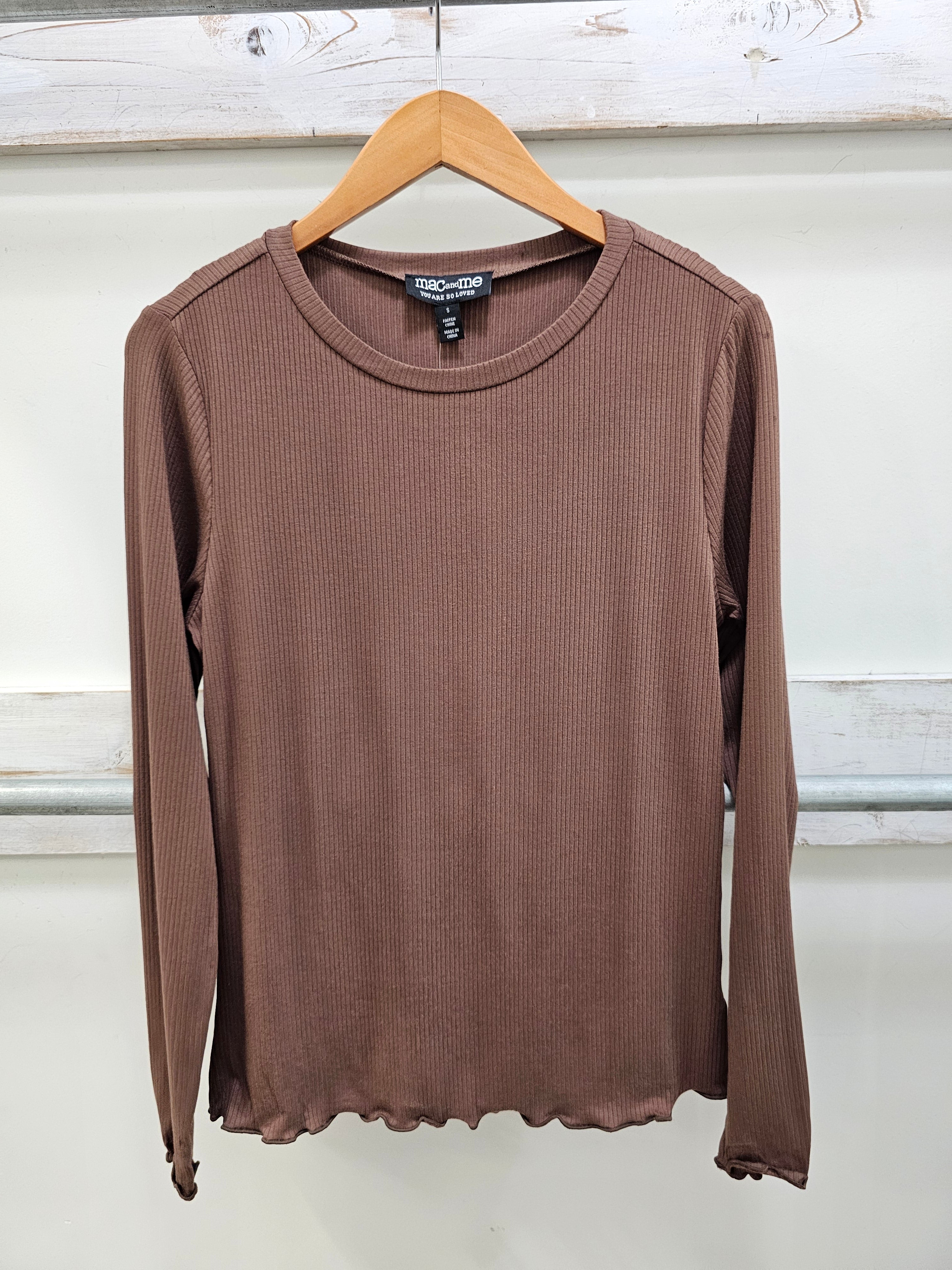 A brown ribbed long-sleeve top hanging on a wooden hanger against a white paneled wall.