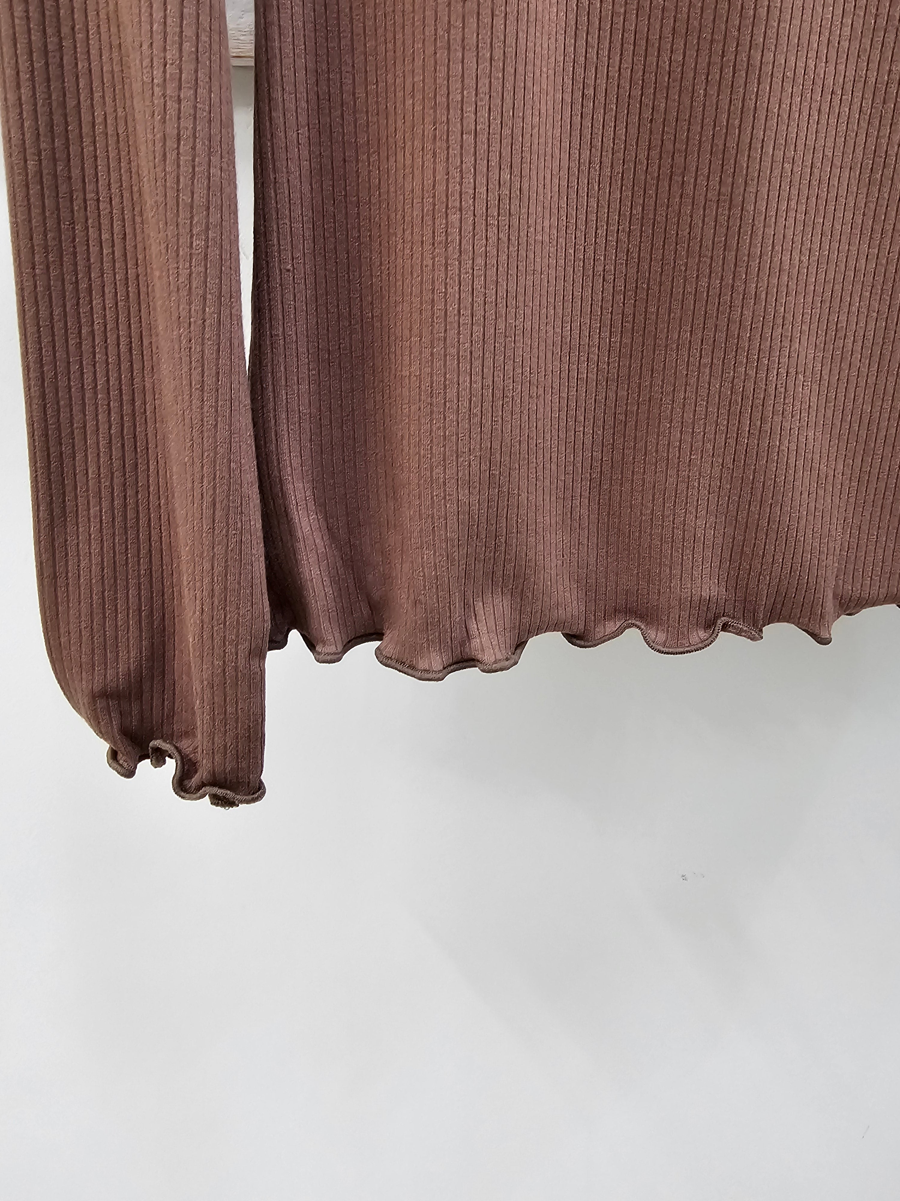Close-up of a ribbed long-sleeve top in a muted dusty rose or mauve-brown color, showing the sleeve cuff and ruffled hem against a plain light background.