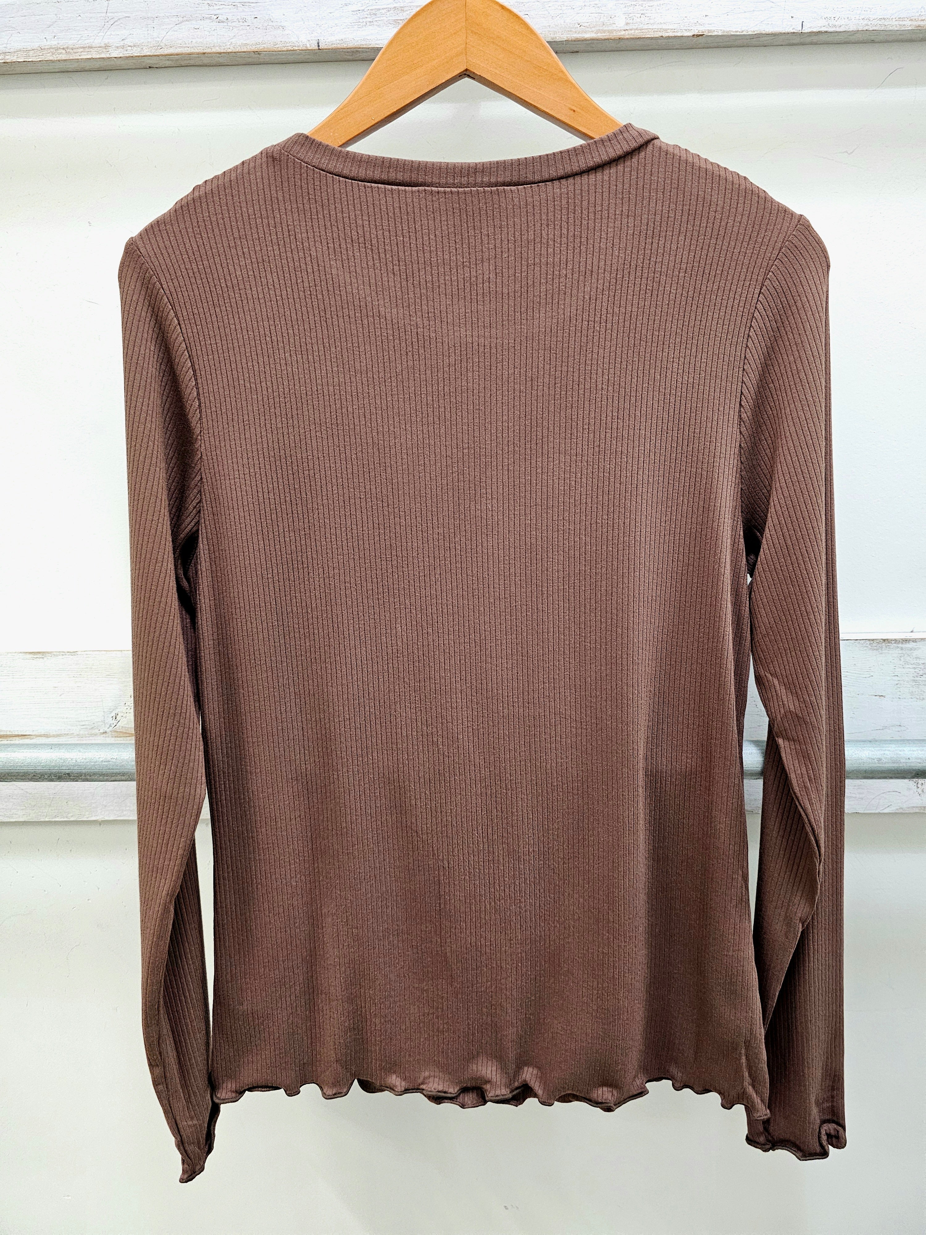 A brown ribbed long-sleeve top hanging on a wooden hanger against a white paneled wall.