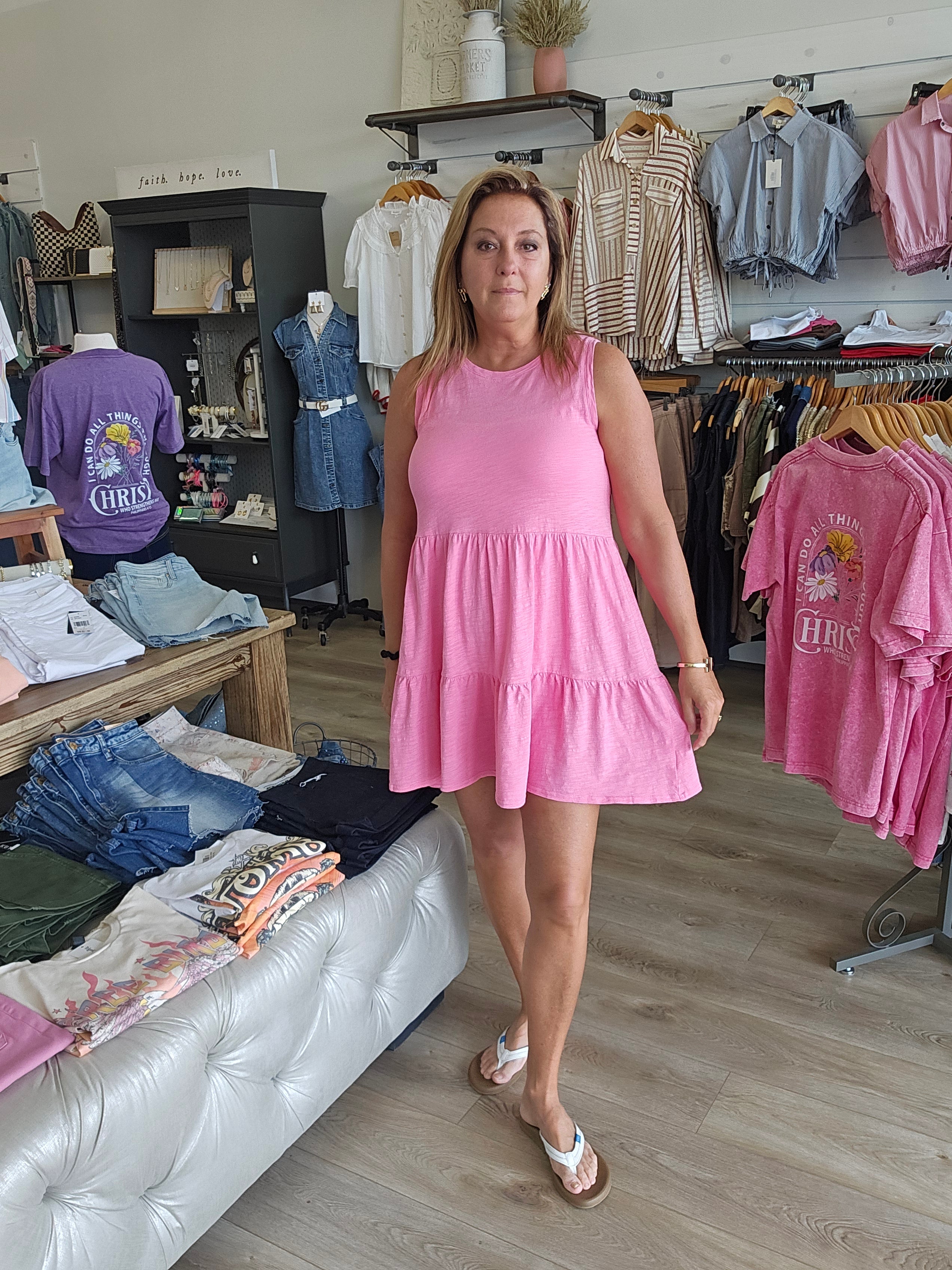 Woman in a pink dress standing in a room with various items on shelves and a couch.